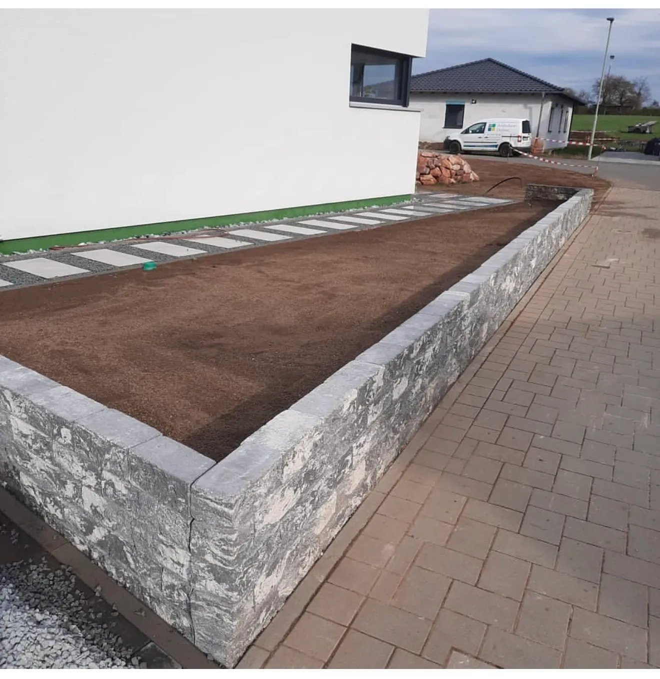 Fertige Natursteinmauer mit Beeteinfassung entlang eines gepflasterten Wegs